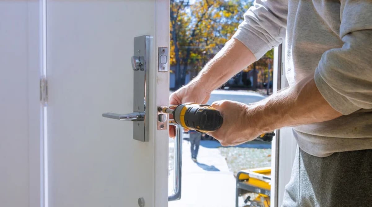Serrurier qui installe une serrure sur une porte d'entrée